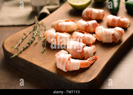 Wooden board with bacon-wrapped shrimps on table, closeup Stock Photo