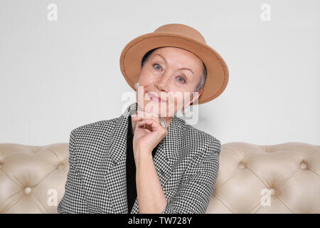 Attractive mature woman sitting on sofa at home Stock Photo