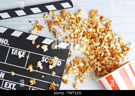 Paper cup with caramel popcorn and movie clapper on wooden background Stock Photo
