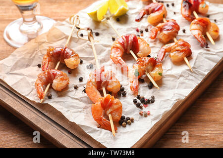 Board with skewered shrimps wrapped in bacon on table Stock Photo