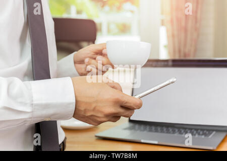 Businessmans hand holding cellphone and cup of coffee in his office. Stock Photo