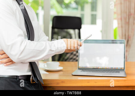 Businessmans hand holding cellphone with laptop on wooden desk. Stock Photo