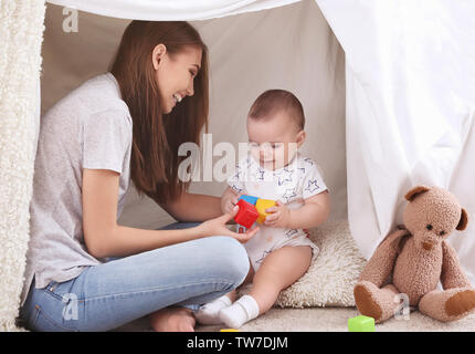 Young mother and cute baby playing in tent at home Stock Photo