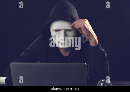 Masked man hacking server in dark room Stock Photo