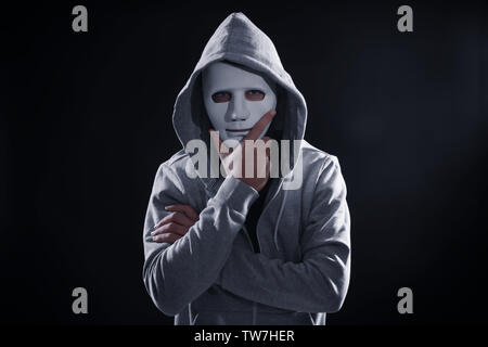 Masked hacker wearing hoodie in darkness Stock Photo