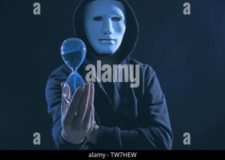 Masked hacker with sand clock in darkness Stock Photo