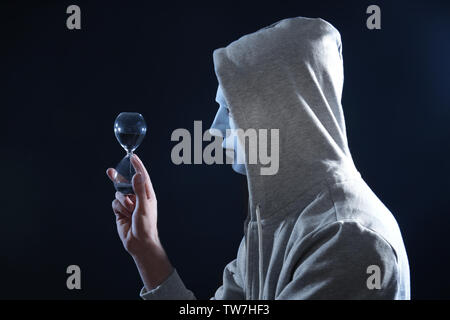 Masked hacker with sand clock in darkness Stock Photo