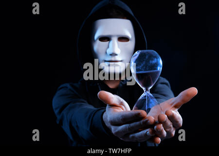 Masked hacker with sand clock in darkness Stock Photo