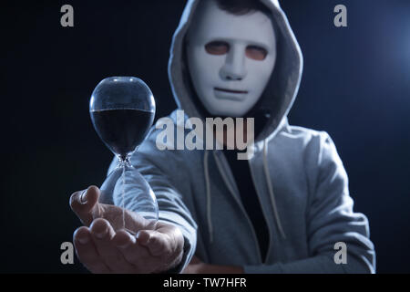 Masked hacker with sand clock in darkness Stock Photo