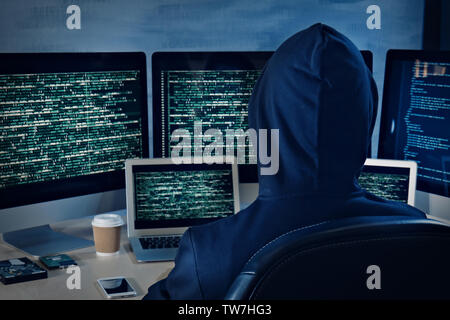 Man in hoodie hacking server at table Stock Photo