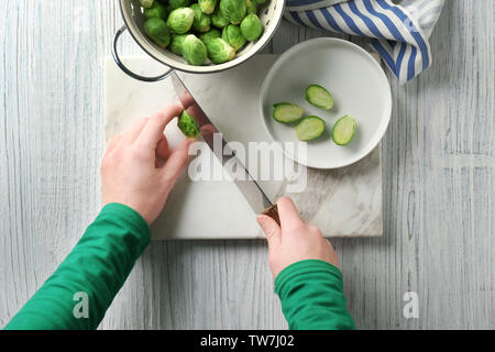 Young woman cutting fresh raw Brussels sprouts on board in kitchen Stock Photo