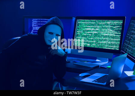 Hacker in mask using computer in dark room Stock Photo