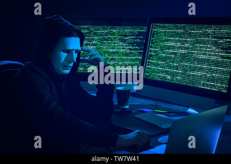 Hacker in mask using computer in dark room Stock Photo