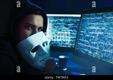 Hacker with mask near computer in dark room Stock Photo