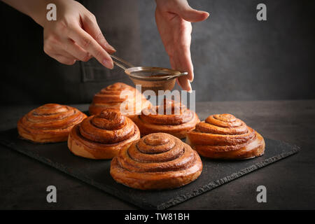 Woman sprinkling sweet rolls with cinnamon on slate plate Stock Photo