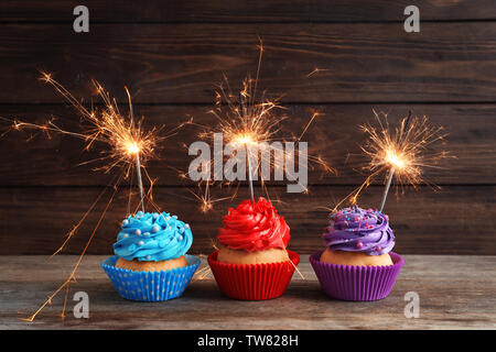 Tasty colorful cupcakes with sparklers on wooden table Stock Photo