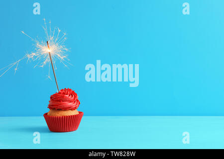Tasty cupcake with sparkler on table against color background Stock Photo