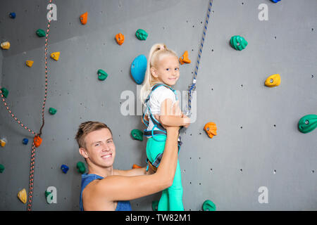 Instructor helping little girl climb wall in gym Stock Photo