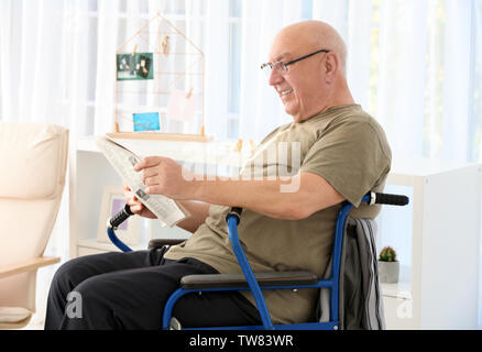 Senior man in wheelchair reading newspaper at care home Stock Photo