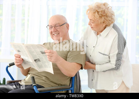 Senior man in wheelchair and woman reading newspaper at care home Stock Photo