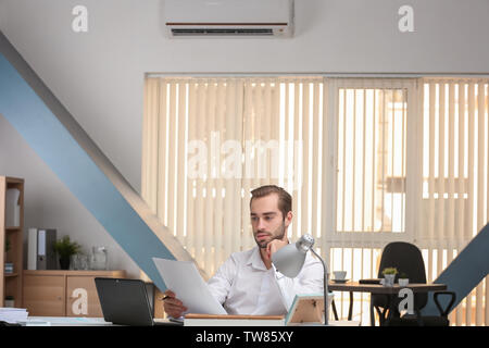 Young man working in office with operating air conditioner Stock Photo