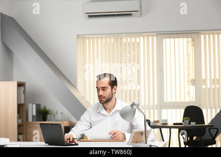 Young man working in office with operating air conditioner Stock Photo