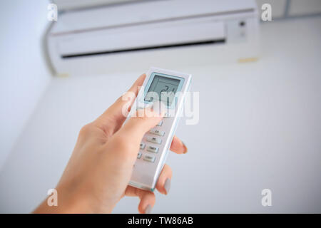 Young woman pointing remote control at air conditioner indoors Stock Photo
