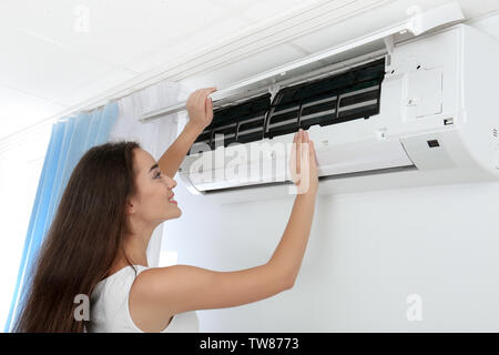 Young woman checking air conditioner at home Stock Photo