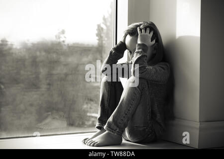 Little sad girl near window. Abuse of children concept Stock Photo