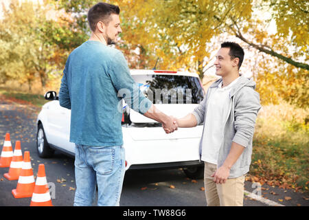 Instructor and young man passed driving license exam, outdoors Stock Photo