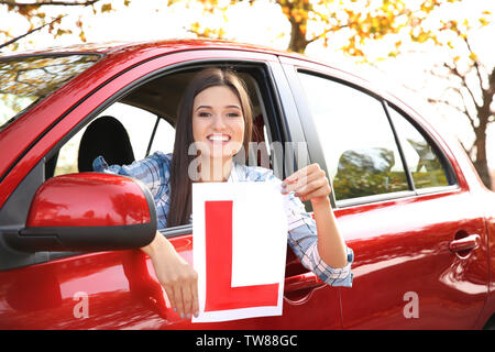 Happy young woman holding learner driver sign in car Stock Photo