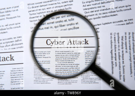 Headline "Cyber attack" in newspaper under magnifying glass, closeup Stock Photo
