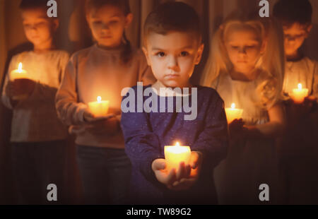 Little children holding burning candles in darkness Stock Photo