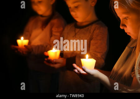 Little children holding burning candles in darkness Stock Photo