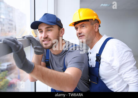 Construction worker with trainee installing window in house Stock Photo