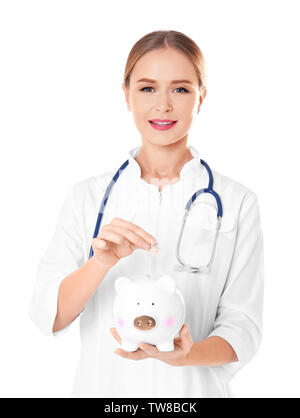Young female doctor putting coin into piggy bank on white background Stock Photo
