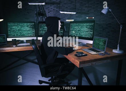 Masked hacker using computer in dark room. Threat of cyber attack Stock Photo