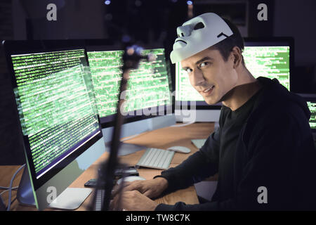 Hacker with mask using computer in dark room. Threat of cyber attack Stock Photo