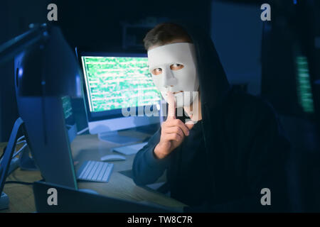 Masked hacker in dark room with computers. Threat of cyber attack Stock Photo