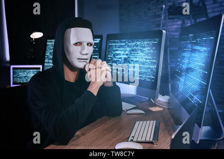 Masked hacker in dark room with computers. Threat of cyber attack Stock Photo