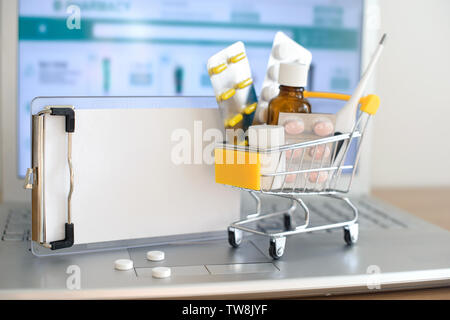 Shopping cart toy with medicaments and paper note in front of laptop screen with pharmacy web site on it. Pills, blister packs, medical bottles, therm Stock Photo