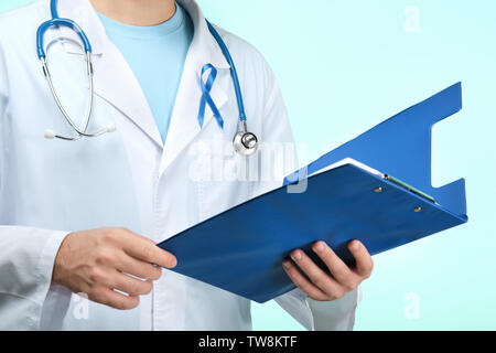 Doctor with symbolic blue ribbon and clipboard on color background. Cancer awareness concept Stock Photo