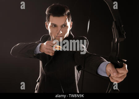 Young businessman practicing archery on dark background Stock Photo