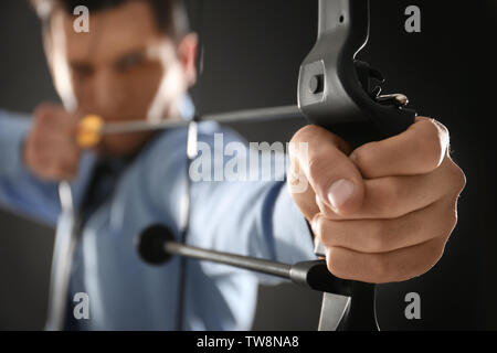 Young businessman practicing archery on dark background Stock Photo