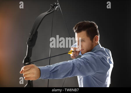 Young businessman practicing archery on dark background Stock Photo