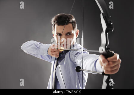 Young businessman practicing archery on dark background Stock Photo