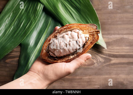 Woman holding cut cocoa pod over table, closeup Stock Photo
