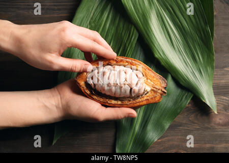 Woman holding cut cocoa pod over table, closeup Stock Photo