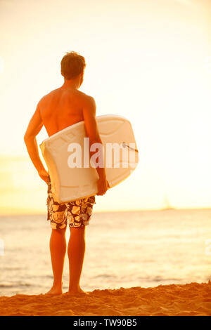 Surfer man on beach at surfing sunset holding bodyboard. Fit male body surfer guy enjoying sunset and bodyboarding on summer holidays vacation on tropical beach. Kaanapali beach, Maui, Hawaii. Stock Photo