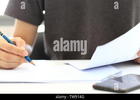man sketching a drawing on blank plain white paper while reading information on another hand. mobile phone placed on white table. drawing and design c Stock Photo